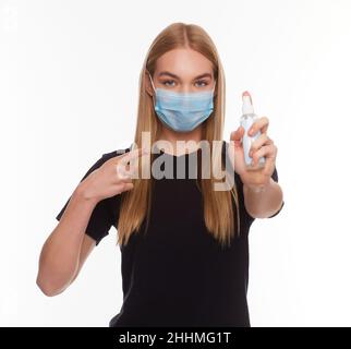 Ein Mädchen in einer medizinischen Maske hält ein Desinfektionsmittel in der Hand. Die zweite Hand zeigt mit einem Zeigefinger auf das Desinfektionsmittel. Hände Waschen Antiseptisch. Corona-Virus Stockfoto