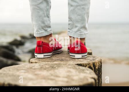 Damenbeine in roten Sneakers und Jeans am Meer. Reisekonzept. Stockfoto