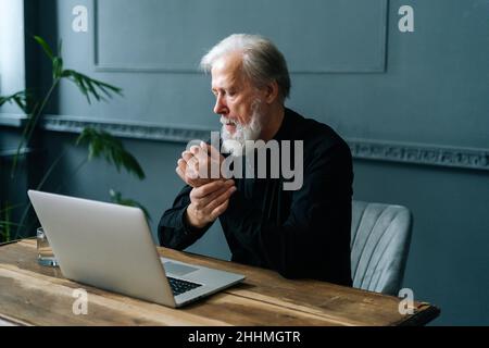 Müde bärtige reife Erwachsene männliche Arbeiten am Laptop Erfahrungen Schmerzen im Handgelenk, Karpaltunnelsyndrom. Stockfoto