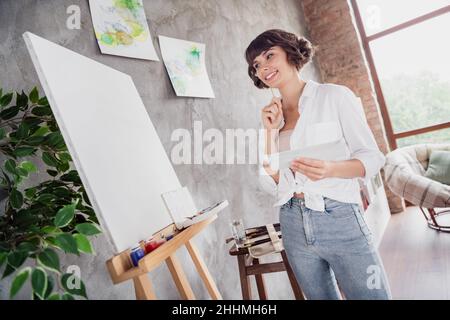 Ganzkörper-Foto von verträumt gesinnten glücklich Frau aussehen Leinwand Maler Bild drinnen Haus Wohnung Stockfoto