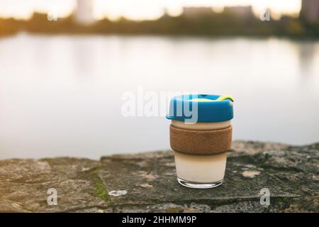 Glasbecher für to-go-Kaffee oder Tee mit Bambus Heißgetränkehalter steht auf Stein im Freien. Wiederverwendbarer Becher für die Umwelt. Bewusster Konsum. Stockfoto