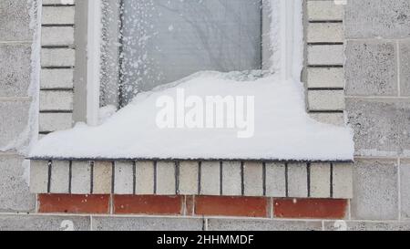 Fenster und Fensterbank mit Schnee bedeckt, kleine Schneeverwehung auf der Fensterbank Stockfoto