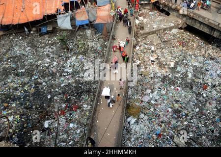 JANUAR 25,2022,DHAKA,BANGLADESH- die Menschen gehen an einer Brücke über ein verschmutztes Gebiet und Kinder gehen über ein verschmutztes Gebiet, während sie Plastikpaten sammeln Stockfoto