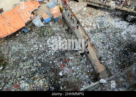 JANUAR 25,2022,DHAKA,BANGLADESH- die Menschen gehen an einer Brücke über ein verschmutztes Gebiet und Kinder gehen über ein verschmutztes Gebiet, während sie Plastikpaten sammeln Stockfoto