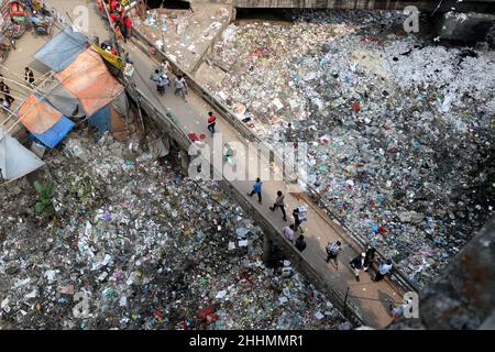 JANUAR 25,2022,DHAKA,BANGLADESH- die Menschen gehen an einer Brücke über ein verschmutztes Gebiet und Kinder gehen über ein verschmutztes Gebiet, während sie Plastikpaten sammeln Stockfoto