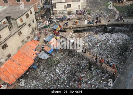 JANUAR 25,2022,DHAKA,BANGLADESH- die Menschen gehen an einer Brücke über ein verschmutztes Gebiet und Kinder gehen über ein verschmutztes Gebiet, während sie Plastikpaten sammeln Stockfoto