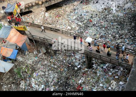 JANUAR 25,2022,DHAKA,BANGLADESH- die Menschen gehen an einer Brücke über ein verschmutztes Gebiet und Kinder gehen über ein verschmutztes Gebiet, während sie Plastikpaten sammeln Stockfoto