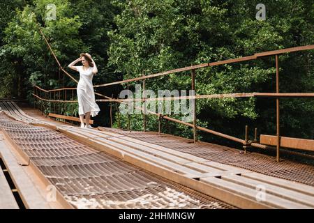 Schöne junge tausendjährige Frau in weißem langen Kleid und Hut geht auf der Brücke und lächelt. Reisekonzept. Stockfoto