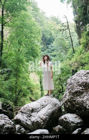 Junge tausendjährige Frau in Kleid und beigem Hut steht im Wald glücklich und entspannt, genießt Natur und Ruhe. Konzept „Travel Alone“. Stockfoto