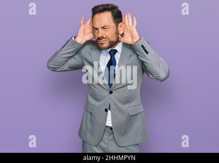 Mann mittleren Alters in Geschäftskleidung versucht, beide Hände auf Ohr Geste hören, neugierig auf Klatsch. Hörproblem, taub Stockfoto