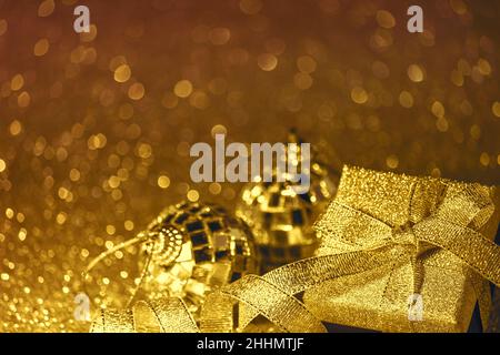 Goldener festlicher Сhristmas-Hintergrund mit Bokeh in Form von Schneeflocken, Geschenkbox und glänzenden Kugeln. Selektiver Fokus, freier Platz für Text. Stockfoto
