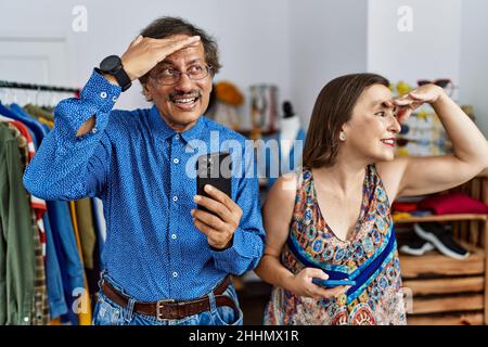 Interrassisches Paar im mittleren Alter im Einzelhandel mit Smartphone sehr glücklich und lächelnd, weit weg mit der Hand über dem Kopf. Suchkonzept. Stockfoto