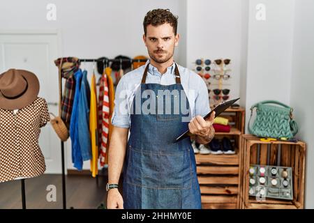 Hübscher junger Mann, der als Manager in der Einzelhandelsboutique arbeitet, skeptisch und nervös, runzelte die Stirn wegen des Problems. Negative Person. Stockfoto