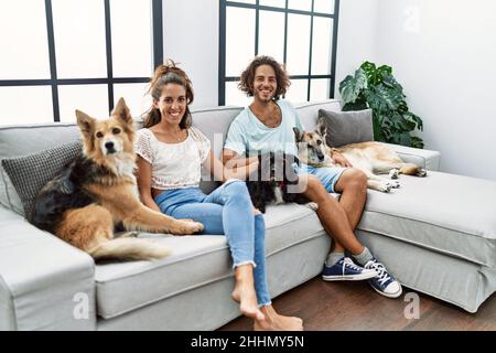 Mann und Frau Paar lächeln selbstbewusst auf dem Sofa mit Hunden zu Hause sitzen Stockfoto