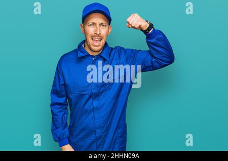 Kahlköpfiger Mann mit Bart trägt Baumeister Jumpsuit Uniform wütend und verrückt Erhöhung Faust frustriert und wütend beim Schreien vor Wut. Wut und aggressiv Stockfoto