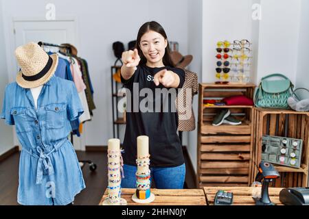 Junge asiatische Frau, die als Managerin in der Einzelhandelsboutique arbeitet, zeigt mit den Fingern auf Sie und die Kamera, lächelt positiv und fröhlich Stockfoto