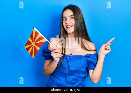 Junge Brünette Teenager hält mazedonische Flagge lächelnd glücklich zeigt mit Hand und Finger zur Seite Stockfoto