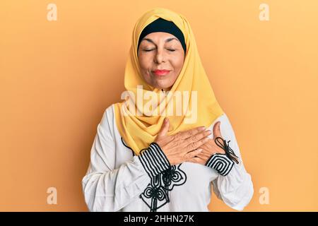 lateinamerikanische Frau mittleren Alters trägt traditionellen islamischen Hijab Schal lächelnd mit Händen auf der Brust mit geschlossenen Augen und dankbare Geste im Gesicht. Gesundheit Co Stockfoto