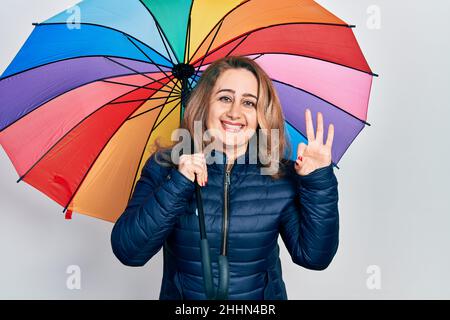 Mittleres Alter kaukasische Frau hält bunten Regenschirm tun ok Zeichen mit Fingern, lächelnd freundlich gestikulieren ausgezeichnete Symbol Stockfoto