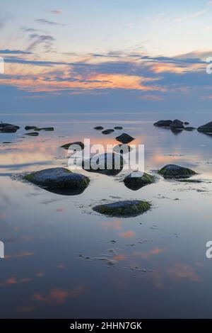 Blaue Stunde nach dem Sonnenuntergang über der felsigen Ostsee kosten. Kleine Steine und große Felsbrocken im Meer. Langzeitbelichtung Stockfoto