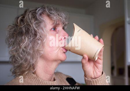 Frau trinkt Kaffee aus einer recycelbaren Butterfly-Tasse aus Papier Stockfoto