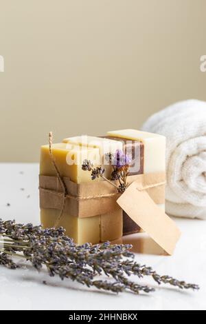 Packung mit vier verschiedenen handgefertigten Naturseifenstäben mit trockenen Lavendelblüten und leerem Etikett. Vertikale Komposition mit Kopierbereich Stockfoto