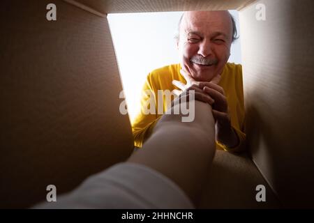 Senior überraschte den Mann beim Auspacken, Öffnen des Kartons und beim Blick nach innen. Jemand greift ihn an. Stockfoto