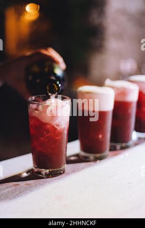 Eine vertikale selektive Fokusaufnahme eines Glases mit einem roten Getränk, das aus einer Flasche gefüllt wird Stockfoto