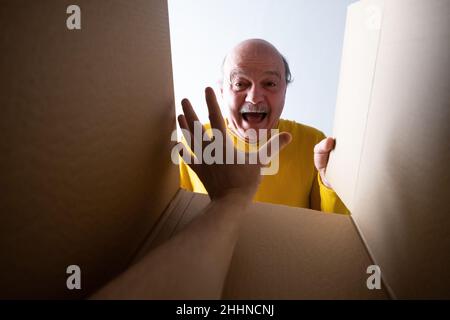 Senior überraschte den Mann beim Auspacken, Öffnen des Kartons und beim Blick nach innen. Jemand greift ihn an. Stockfoto
