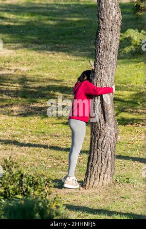 Ein Mädchen spielt sich in einem öffentlichen Park versteckt und versteckt sich hinter einem Kiefernstamm Stockfoto