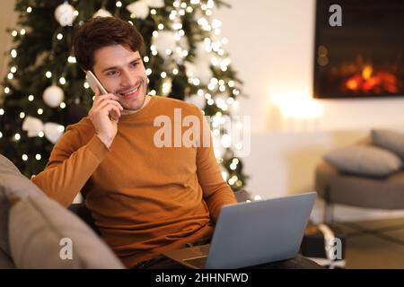 Fröhlicher Mann, der mit dem pc am Handy arbeitet und spricht Stockfoto