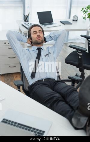 Sicherheitsmann sitzt mit Beinen auf dem Schreibtisch und schläft im Büro Stockfoto