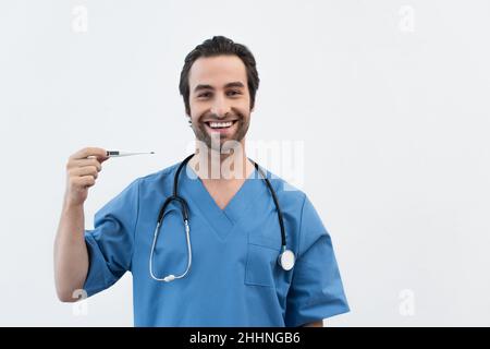 Fröhlicher Arzt in blauer Uniform mit elektronischem Thermometer isoliert auf grau Stockfoto