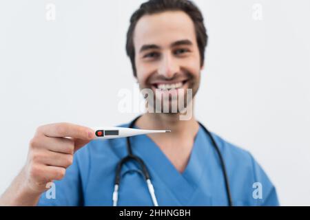 Verschwommener Arzt mit elektronischem Thermometer lächelt auf verschwommenem Hintergrund isoliert auf grau Stockfoto
