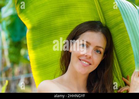 Schöne junge kaukasische Frau Porträt in der Nähe Bananenpalme Blätter tropischen Pflanzen im Dschungel. Hautpflege und natürliches organisches Beauty-Konzept. Stockfoto