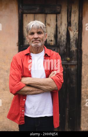Porträt eines selbstbewussten kaukasischen reifen Mannes, der mit gekreuzten Armen gegen das Haus steht. Lifestyle und einfaches Wohnkonzept. Stockfoto