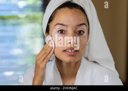 Nahaufnahme Porträt der biracial junge Frau im Bademantel Anwendung Creme auf das Gesicht. Unverändert, Routine, Lebensstil, Hautzustand und Vitiligo Konzept. Stockfoto