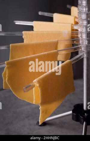 Nahaufnahme von frischer, hausgemachter Pasta, die auf einem Pasta-Trocknergestell hängt und für Lasagne verwendet werden kann. Selektiver Fokus Stockfoto