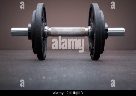 Eine Hantelstange mit Hantelscheiben auf dem Boden im Fitnessstudio. Bodybuilding-Ausrüstung auf einem sauberen Hintergrund mit leerem Platz für Text Stockfoto