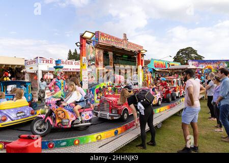 Fun Fair UK, Eltern und Kinder; Kinder auf einer Fahrt auf dem Messegelände in der Sommersonne, Harpenden Hertfordshire UK Stockfoto