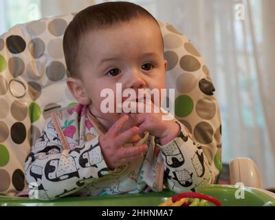 Baby Junge saß im Hochstuhl essen, Großbritannien Stockfoto