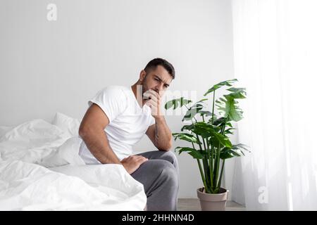 Trauriger nachdenklicher junger kaukasischer muskulöser Mann sitzt auf weißem Bett und leidet unter Schmerzen, Stress und Problemen Stockfoto