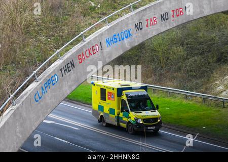 Weymouth, Dorset, Großbritannien. 25th. Januar 2022. Ein Krankenwagen des NHS fährt am A354 in Weymouth in Dorset unter einer Brücke durch, auf der eine Graffiti-Nachricht geschrieben wurde, in der stand: „klatscht dann geplündert! NHS100K Keine Jabs Keine Jobs! Die Botschaft ist erschienen, da die Frist für die obligatorische Covid-Impfung der NHS-Mitarbeiter durch die Regierungen mit der Frist für den ersten Jab am 3rd. Februar und für die vollständige Impfung bis zum 1st. April 2022 anrückt. Bildnachweis: Graham Hunt/Alamy Live News Stockfoto