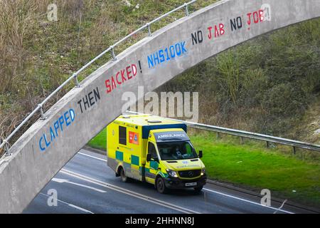 Weymouth, Dorset, Großbritannien. 25th. Januar 2022. Ein Krankenwagen des NHS fährt am A354 in Weymouth in Dorset unter einer Brücke durch, auf der eine Graffiti-Nachricht geschrieben wurde, in der stand: „klatscht dann geplündert! NHS100K Keine Jabs Keine Jobs! Die Botschaft ist erschienen, da die Frist für die obligatorische Covid-Impfung der NHS-Mitarbeiter durch die Regierungen mit der Frist für den ersten Jab am 3rd. Februar und für die vollständige Impfung bis zum 1st. April 2022 anrückt. Bildnachweis: Graham Hunt/Alamy Live News Stockfoto