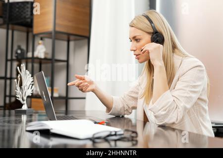 Charmante Geschäftsfrau, Lehrerin, Online-Tutorin trägt Headset mit Laptop für Videokonferenzen, Online-Unterricht, führt Webinar im Büro sitzen. Weibliche Unterstützerin Stockfoto