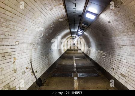 Blick auf einen schmalen Fußgängertunnel mit Menschen, die in weiter Ferne laufen, aufgenommen am Greenwich Foot Tunnel unter der Themse, 30th. Dezember 2022 Stockfoto