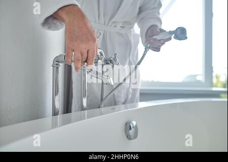 Mann in einem weißen Frottee-Bademantel, der die Badewanne mit Wasser füllte Stockfoto