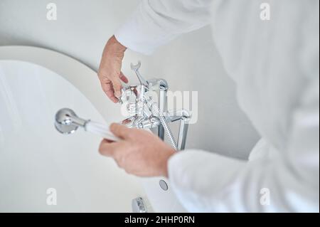 Person in einem weißen Bademantel, der das Bad mit Wasser füllt Stockfoto