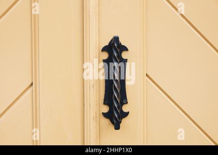 Heller Holzeingang mit antikem Türgriff. Details der verzierten gelb bemalten Tür. Türknauf aus Vintage-Eisen. Klassischer Stil mit geraden Linien. Stockfoto