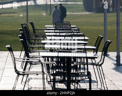 25. Januar 2021, Baden-Württemberg, Stuttgart: Vor dem landtag stehen Tische eines Straßencafés in der Sonne, im Hintergrund laufen Menschen durch einen Park. Foto: Bernd Weißbrod/dpa Stockfoto